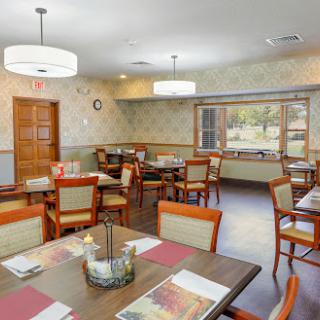 A spacious and inviting dining area set up for meals, featuring wooden tables and chairs with a warm color palette.