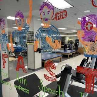 A gym with colorful illustrations and motivational text on the windows, overlooking exercise equipment inside.