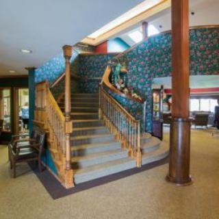 A cozy interior space featuring a central wooden staircase with decorative wallpaper and carpeted steps.