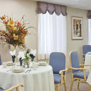 A well-decorated dining room with neatly arranged tables and chairs, featuring floral centerpieces and elegant curtains.