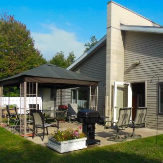 A backyard patio setup with a gazebo, outdoor furniture, and a grill.