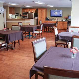 A dining area with neatly arranged tables and chairs, featuring a television on the wall.
