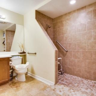 An accessible bathroom with a walk-in shower, equipped with grab bars and a wooden stool.