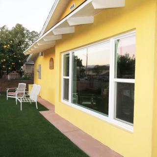 Sunny view of a house with a yellow exterior, featuring large windows and a grassy lawn.