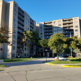 A multi-story apartment building surrounded by greenery and a clear blue sky.
