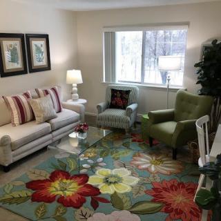A cozy living room with colorful floral decor, featuring a sofa, armchairs, and bright lighting.