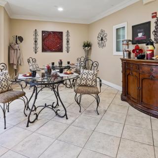 A stylish dining room featuring a glass table and wrought iron chairs set on a tiled floor, with decorative art pieces and a wooden sideboard.