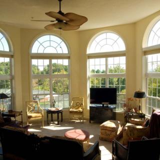 A sunlit living room with arched windows, elegant furniture, and a ceiling fan.