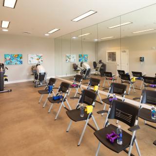 A spacious exercise room with chairs and fitness equipment lined up in front of large mirrors.
