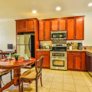 A modern kitchen with wooden cabinets and stainless steel appliances, adjacent to a dining area with a round table and chairs.