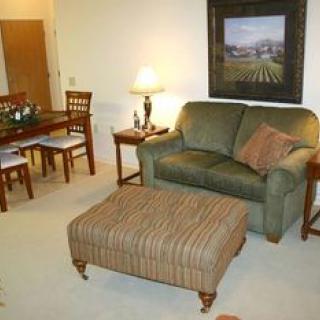 A cozy living room with a green sofa and ottoman, adjacent to a small dining area.