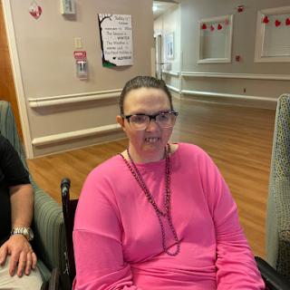 A woman in a pink sweater seated and smiling indoors.