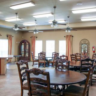 A spacious dining room with wooden tables and chairs, illuminated by natural light from several windows.
