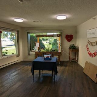 A spacious and well-lit indoor room featuring a black table, large windows, and decorative elements.