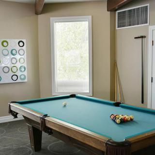 A well-lit game room featuring a pool table with cues and a decorative wall art.