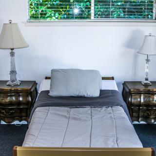 A neatly arranged bed between two nightstands with lamps, underneath a bright window.
