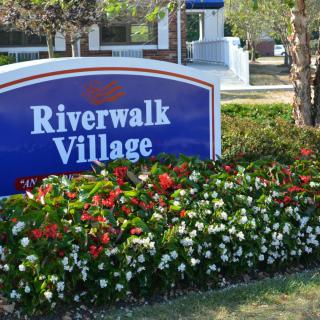 A sign for Riverwalk Village surrounded by a colorful flower garden.
