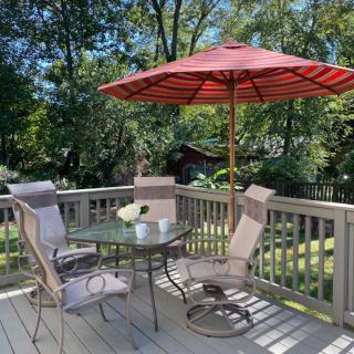 A cozy outdoor patio with a glass table, chairs, and a red umbrella on a sunny day.