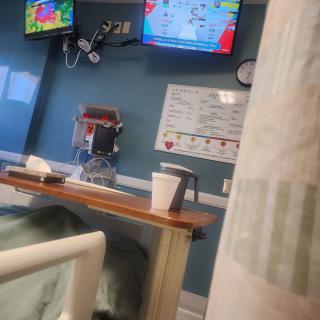 A view from a hospital bed showing medical equipment and a television on the wall.