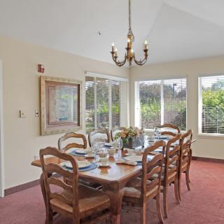 A bright dining room with a large wooden table, surrounded by chairs and illuminated by a classic chandelier.