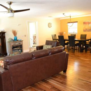 A spacious living and dining area featuring a brown leather sofa, elegant dining table, and warm wooden flooring.