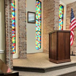 A church interior featuring a pulpit, colorful stained glass windows, and an American flag.