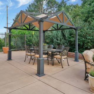 A cozy patio setup featuring a metal gazebo with a dining table and chairs underneath.