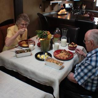 An elderly couple enjoying a meal together at a dining table in their home.