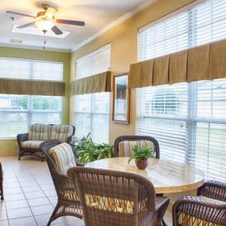 A cozy sunroom with large windows, wicker furniture, and a ceiling fan.