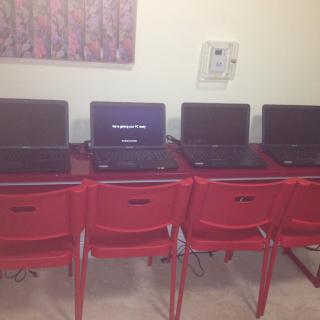 A row of laptops placed on desks with red chairs, likely in a classroom setting.