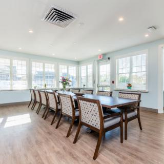 A bright dining room with a long table and multiple chairs surrounded by large windows.