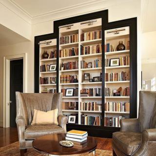 A cozy living room with a large bookshelf filled with books and decor, accompanied by two comfortable armchairs and a wooden coffee table.