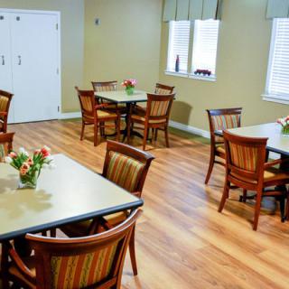 A neatly arranged dining room with wooden flooring and tables set with flowers.