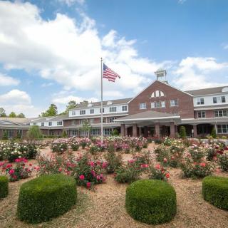 A picturesque view of a building surrounded by a well-maintained garden with blooming flowers and a flagpole.