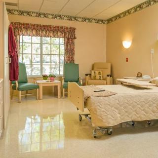 A clean and organized hospital room with a bed, chairs, and a large window.