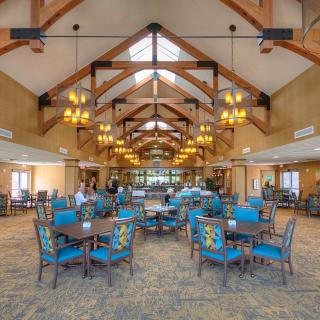 A spacious dining area with blue chairs and wooden tables under a vaulted ceiling adorned with chandeliers.