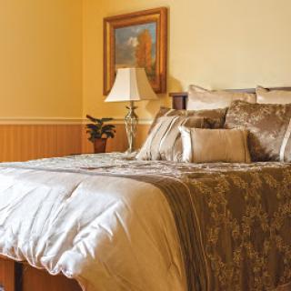 A cozy bedroom with a neatly made bed, decorative pillows, and a lamp beside a painting.