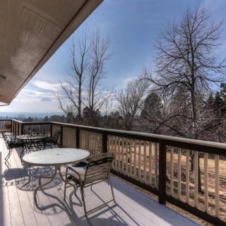 A spacious outdoor deck with tables and chairs overlooking a scenic view with trees and clear skies.
