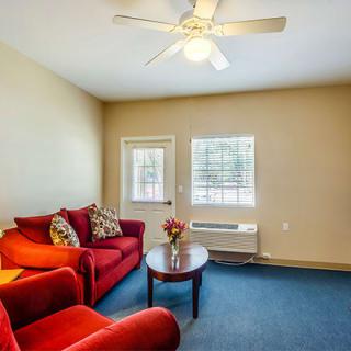 A cozy living room with a red couch and armchair, featuring a coffee table and a ceiling fan overhead.