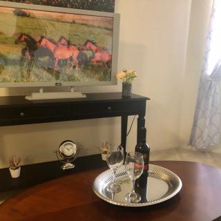 A cozy living room setup featuring a painting of horses on the wall, a TV stand, and a table with a wine set.