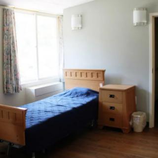 A simple bedroom with a single bed, wooden furniture, and a window letting in natural light.