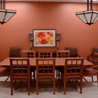 A cozy dining room featuring a large wooden table surrounded by chairs, set against an orange wall with decorative lighting and artwork.