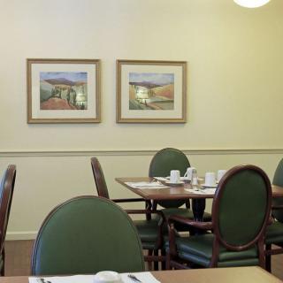A cozy dining room with green chairs and neatly set tables featuring framed paintings on the wall.