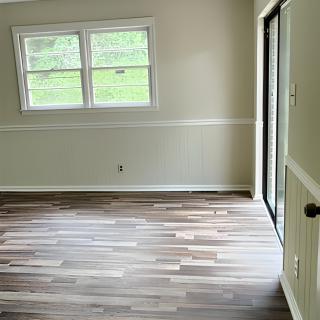 A bright room with wooden flooring and natural light coming through the windows and sliding door.
