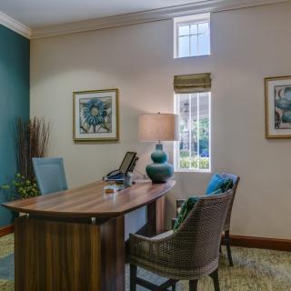 A cozy office setup featuring a wooden desk with a lamp and two chairs, accented by artwork on the walls.