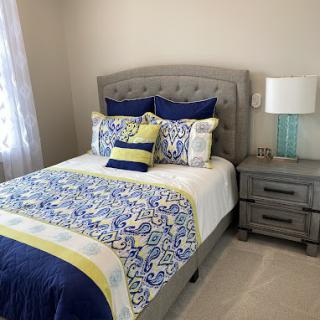 A cozy bedroom with a neatly made bed featuring colorful pillows and a patterned comforter, alongside a nightstand with a lamp.