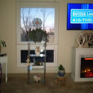 A cozy living room setup featuring a window with plants, a shelf, and a television displaying information.