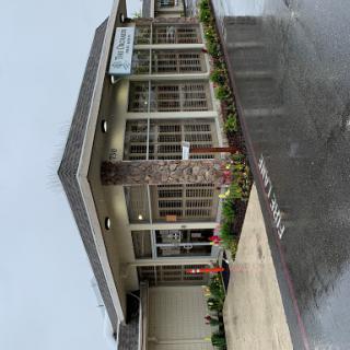 A modern commercial building entrance surrounded by greenery on a rainy day.