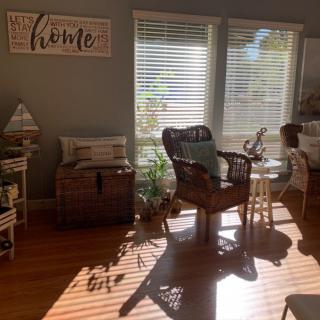 A cozy living room filled with natural light, featuring rattan furniture and indoor plants.