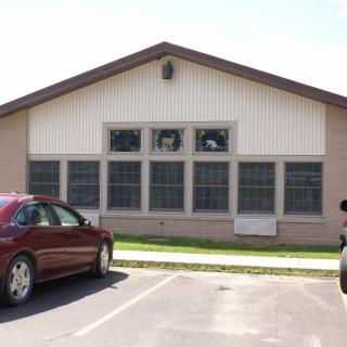 A small building with a parking lot and parked cars on a sunny day.